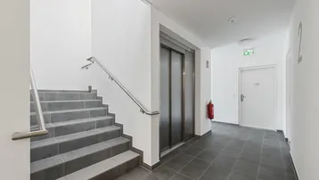 Heller Treppenaufgang mit Fliesenboden und Zugang zum Aufzug in einem Neubau.