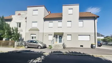 Ansicht des Mehrfamilienhauses von der Straße mit Parkmöglichkeiten und gepflegter Fassade.