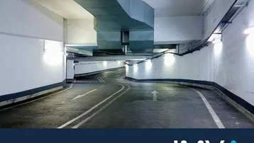 Geschwungene Rampe einer Tiefgarage mit klaren Fahrbahnmarkierungen, Beleuchtung und Lüftungssystem.