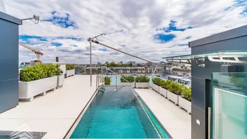Exklusive Dachterrasse mit schmalem Pool, Pflanzenkübeln und weitem Stadtblick unter bewölktem Himmel.