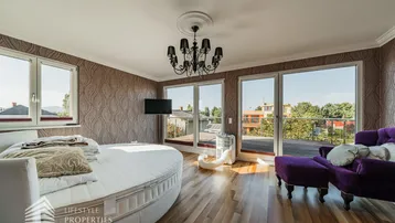 Helles Schlafzimmer mit rundem Bett, großen Fenstern und direktem Zugang zur sonnigen Dachterrasse.