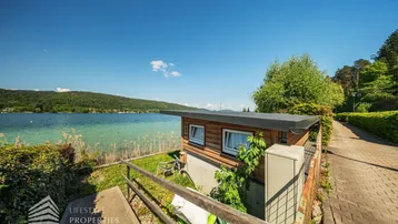 Kleines Holzhaus am Seeufer mit Zugang zum Wasser und umgebender Natur.