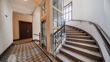 Elegantes Treppenhaus mit historischem Fliesenboden und modernem Glasaufzug in einem Altbau.