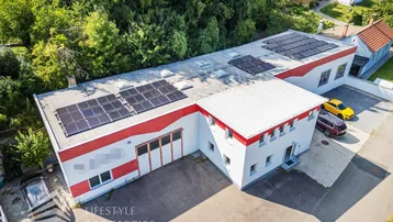 Luftaufnahme eines Gewerbegebäudes mit Solarpaneelen auf dem Dach und umliegender grüner Landschaft.