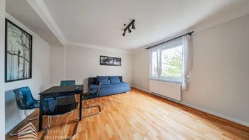 Helles Wohnzimmer mit Parkettboden, einem Sofa und einem kleinen Esstisch am Fenster.