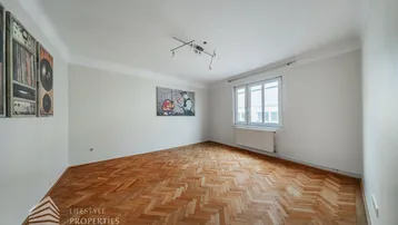 Helles, leeres Wohnzimmer mit Fischgrätparkettboden und einem Fenster, das viel Tageslicht hereinlässt.