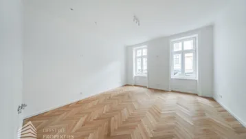 Helles, leeres Zimmer mit Fischgrätparkett und hohen Fenstern, bereit zur individuellen Gestaltung.