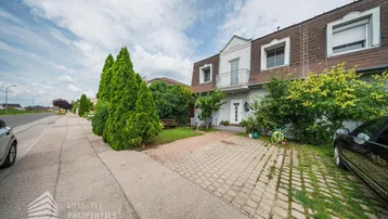 Vorderansicht des Hauses mit gepflasterter Einfahrt, begrüntem Vorgarten und Mansarddach.