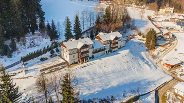 Luftaufnahme eines Gebäudekomplexes in verschneiter Berglandschaft mit umliegenden Wäldern.