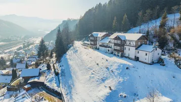 Gebäudekomplex in winterlicher Umgebung, eingebettet in eine hügelige Landschaft mit Fernblick auf das Tal.