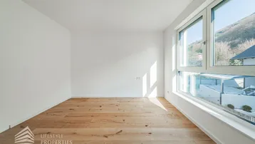 Helles Schlafzimmer mit Holzboden und großen Fenstern, die einen weiten Blick auf die Berge bieten.