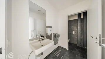 Modernes Badezimmer mit Waschbecken, Spiegel und Handtrockner, gefliest mit dunklen Steinplatten.