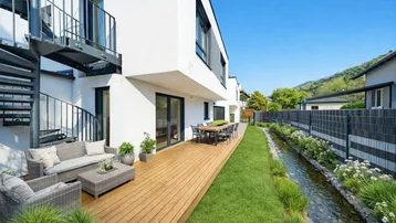 Moderne Terrasse mit Holzboden, Sitzgelegenheiten und Blick auf einen kleinen Bachlauf.