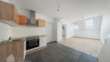 Heller offener Wohnbereich mit integrierter Küche, Dachschrägen und Parkettboden.