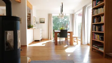 Heller offener Wohn- und Essbereich mit Kaminofen, Holzboden und großen Fenstern zum Garten.