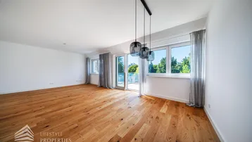 Helles Wohnzimmer mit Holzboden, großen Fenstern und Zugang zu einem Außenbereich.