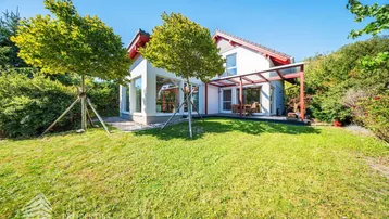 Modernes Einfamilienhaus mit großem Garten und überdachter Terrasse unter blauem Himmel.