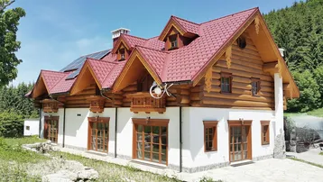 Traditionelles Holzhaus mit weißer Fassade, rotem Dach und rustikalen Holzelementen in sonniger Umgebung.