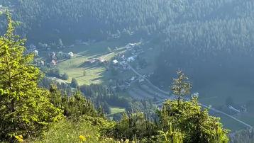 Weitläufiger Blick über ein grünes Tal mit bewaldeten Bergen und kleinen Siedlungen.