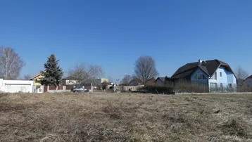 Weitläufiges Grundstück mit trockenem Gras und umliegenden Wohnhäusern unter klarem blauem Himmel.