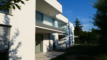 Moderne weiße Fassade eines Neubaus mit Balkonen und Terrassenzugang im Sonnenlicht.