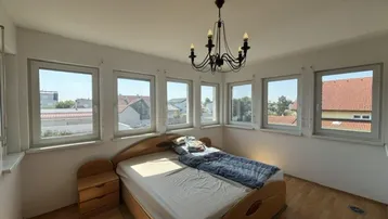 Schlafzimmer mit vielen Fenstern, Holzbett und Blick auf die Umgebung.
