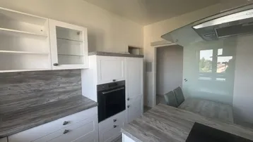 Moderne Küche mit weißen Schränken, Holzoptik-Arbeitsplatten und integriertem Essbereich am Fenster.