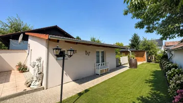 Gepflegter Gartenbereich mit Rasenfläche, kleiner Terrasse und dekorativer Außenbeleuchtung am Haus.