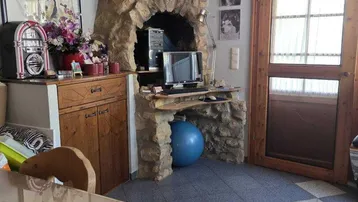 Rustikaler Wohnbereich mit Steinkamin, Holzbalkendecke und gemusterten Fliesen.