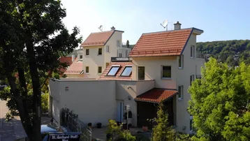 Mehrere moderne Gebäude mit hellen Fassaden und roten Ziegeldächern in einer grünen Umgebung.