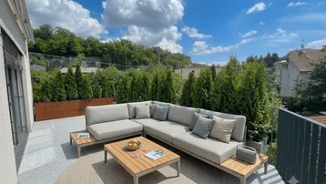 Große, möblierte Terrasse mit bequemen Lounge-Möbeln und Blick ins Grüne unter blauem Himmel.
