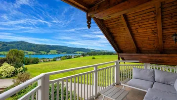 Möblierter Balkon mit Holzbalkendecke und weitem Blick auf den See und die grüne Landschaft.