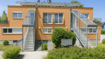Moderne Wohnanlage mit orangefarbener Fassade, Außentreppen und Balkonen.