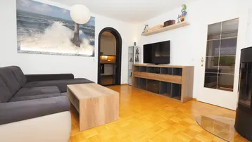 Helles Wohnzimmer mit Parkettboden, gemütlichem Sofa und Zugang zur Küche durch einen Bogen.