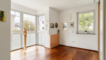 Heller Raum mit großen Fenstern, Holzboden und Zugang zu einem französischen Balkon.