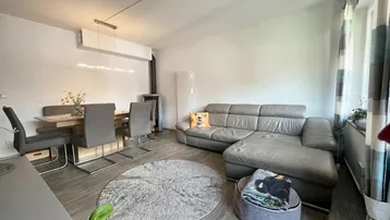 Helles Wohn- und Esszimmer mit modernem Sofa, Esstisch und einem Kaminofen.