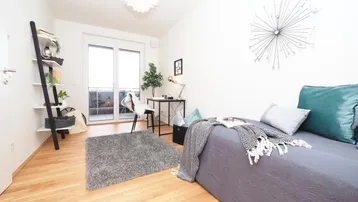 Helles Schlafzimmer mit Holzboden, Schreibtisch und Zugang zu einem französischen Balkon.