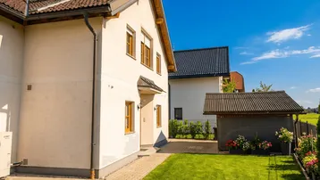 Modernes Einfamilienhaus mit gepflegtem Rasen und kleinem Gartenhaus unter blauem Himmel.