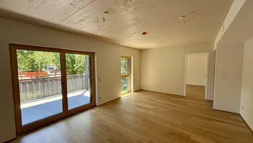 Helles Zimmer mit Holzboden und Zugang zu einem Balkon, ideal als Wohnbereich in einem Neubau.