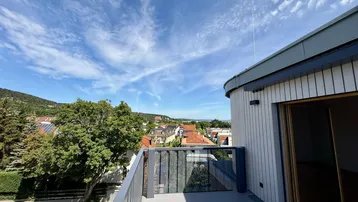 Heller Balkon mit modernem Geländer und weitem Blick über die Dächer und grüne Hügel.
