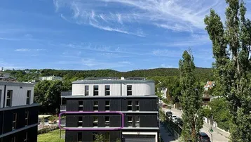 Modernes Mehrfamilienhaus mit schwarzer und weißer Fassade, umgeben von Grünflächen und Bäumen, mit Blick auf die Landschaft.