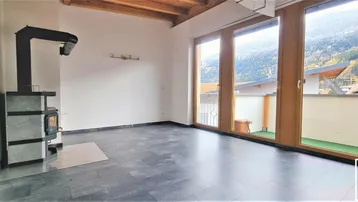 Helles Wohnzimmer mit Kaminofen, großen Fenstern, Holzbalkendecke und Bergblick.