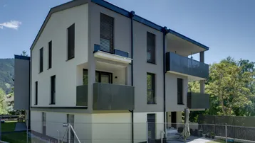 Modernes Mehrfamilienhaus mit Balkonen und kleiner Gartenfläche in alpiner Umgebung.
