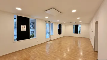 Geräumiger, heller Innenraum mit Holzfußboden und vielen Fenstern, ideal für gewerbliche Nutzung.
