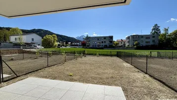 Blick von der Terrasse über den Garten auf die umliegende Bebauung und die Berge im Hintergrund.
