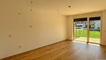 Heller Wohnraum mit Holzboden und Zugang zu einem Balkon mit Blick ins Grüne.