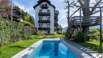 Großzügiger Gartenbereich mit Pool und Baumhaus vor beeindruckender Bergkulisse.