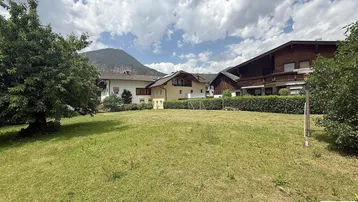 Großes grünes Grundstück mit umliegenden Häusern und beeindruckendem Bergblick unter bewölktem Himmel.