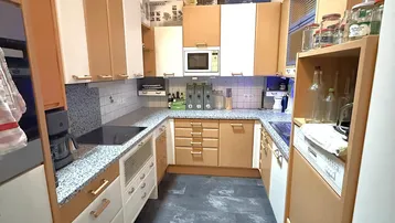 Funktionale Küche mit Holzschränken, Granit-Arbeitsplatten und integrierten Geräten.