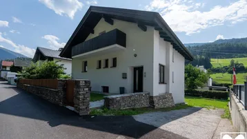 Modernes Einfamilienhaus mit weißer Fassade, schwarzem Dach und kleinem Vorgarten.